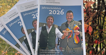 Jahresrückblick wird in die Luft gehalten. Im Hintergrund ist Herbstlaub zu sehen.