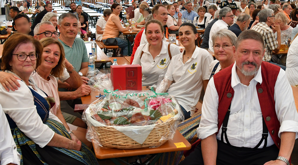 Eine Gruppe von Menschen im Festzelt. Auf der Biertischgarnitur ein Presentkorb.