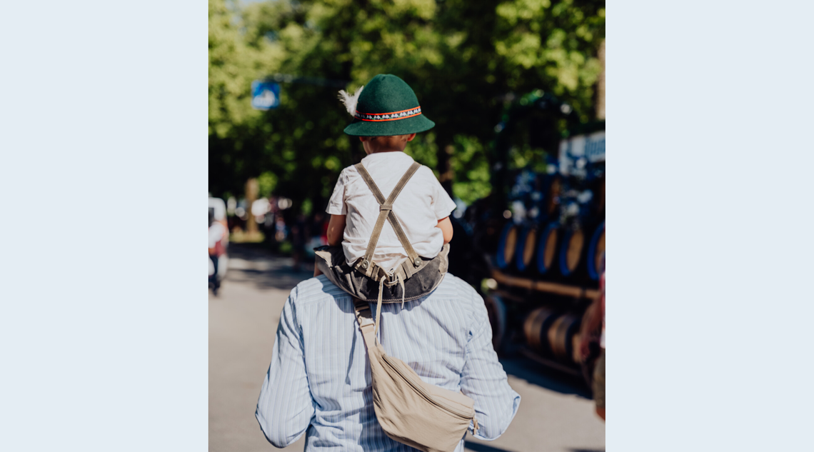 Ein Mann trägt einen kleinen Jungen in Lederhosen und Hut auf seinen Schultern.
