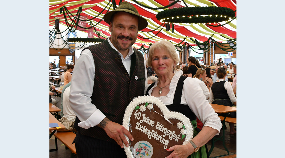 Zwei Personen im Festzelt halten ein großes Lebkuchenherz in den Händen.