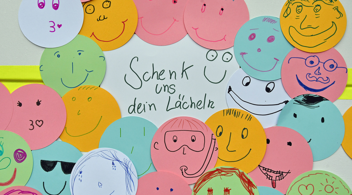 Selbstgemalte lächelnde Gesichter mit der Überschrift "Schenk uns ein Lächeln"