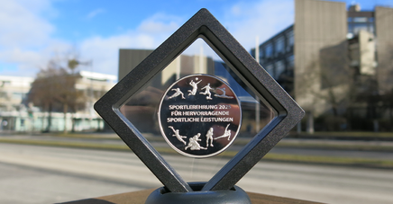 Medaille einer vergangenen Sportlerehrung. Im Hintergrund das Rathaus.