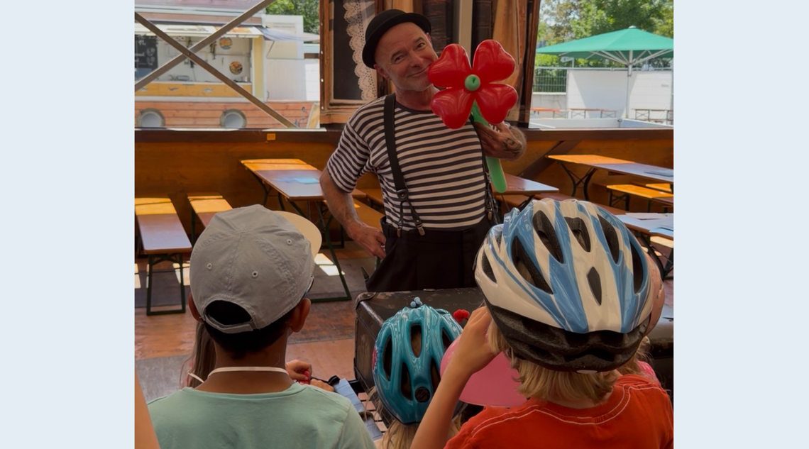 Eine Person steht mit einer Blume aus Luftballonen vor einer Kindergruppe.