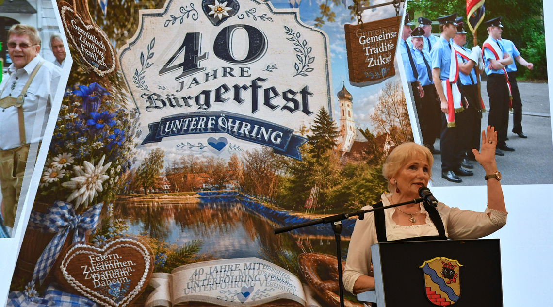 Eine Frau am Rednerpult im Hintergrund eine Präsentation über 40 Jahre Bürgerfest Unterföhring.